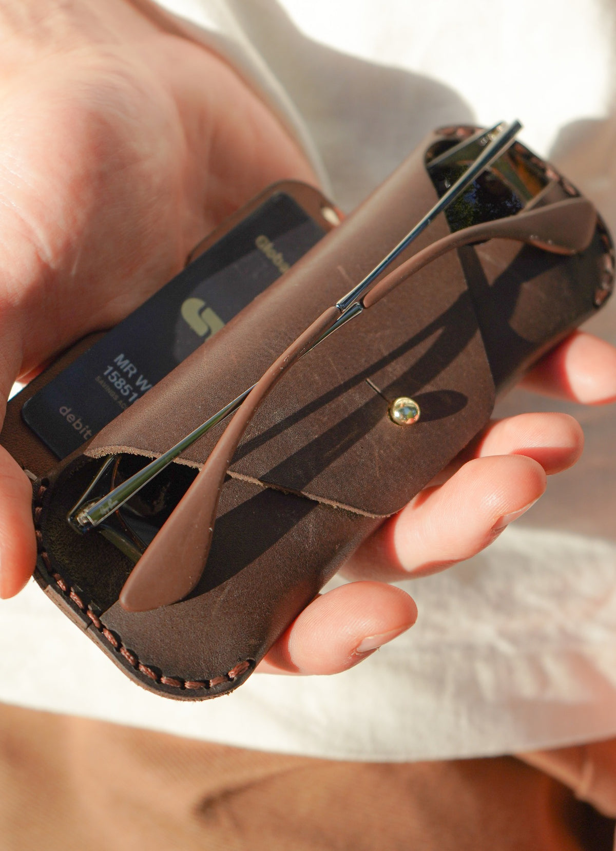 Hand holding a brown leather case with a device inside, blurred background