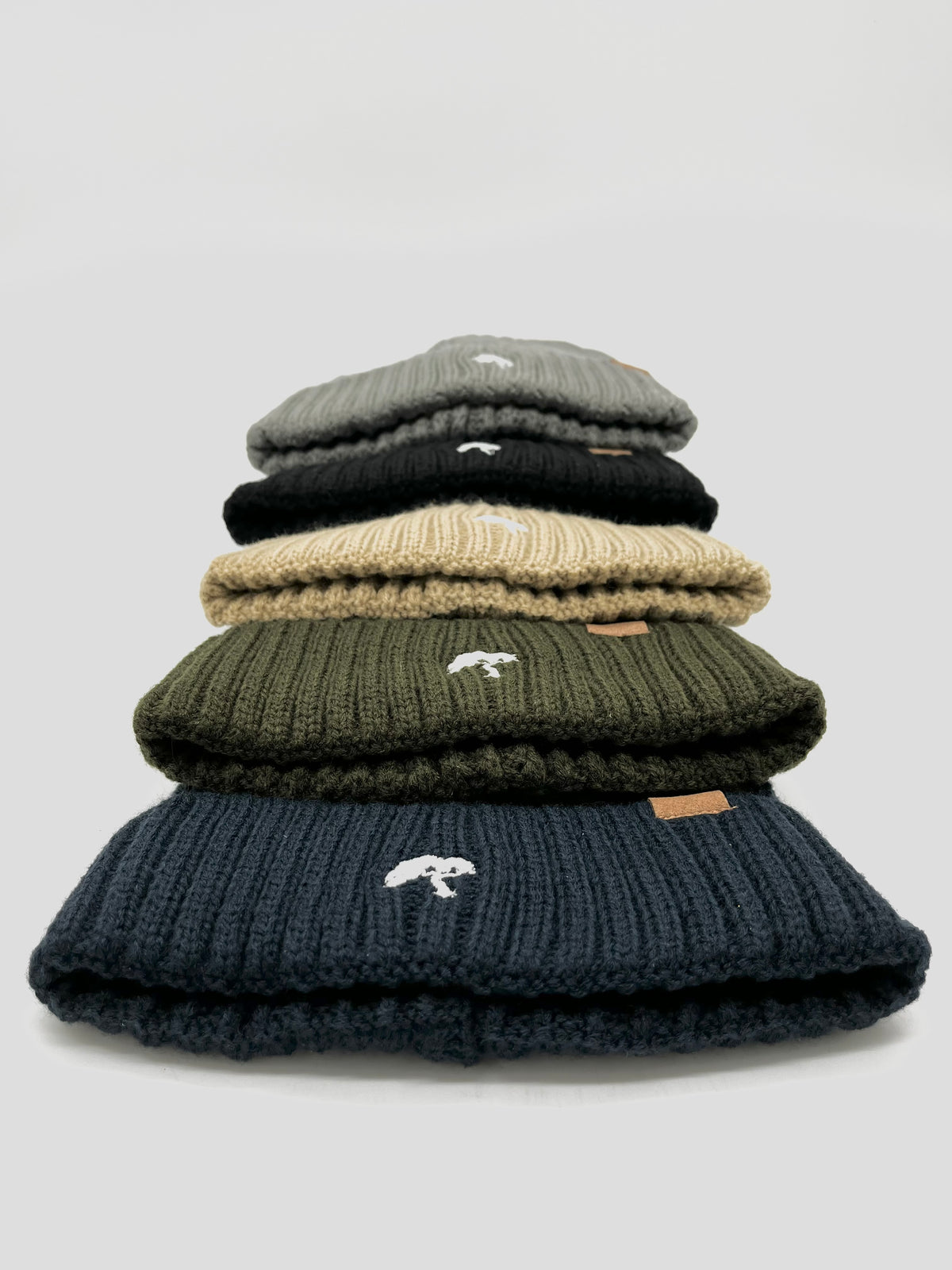 A stack of beanies in beige, black, and green colors, with a visible brand tag on all of them.