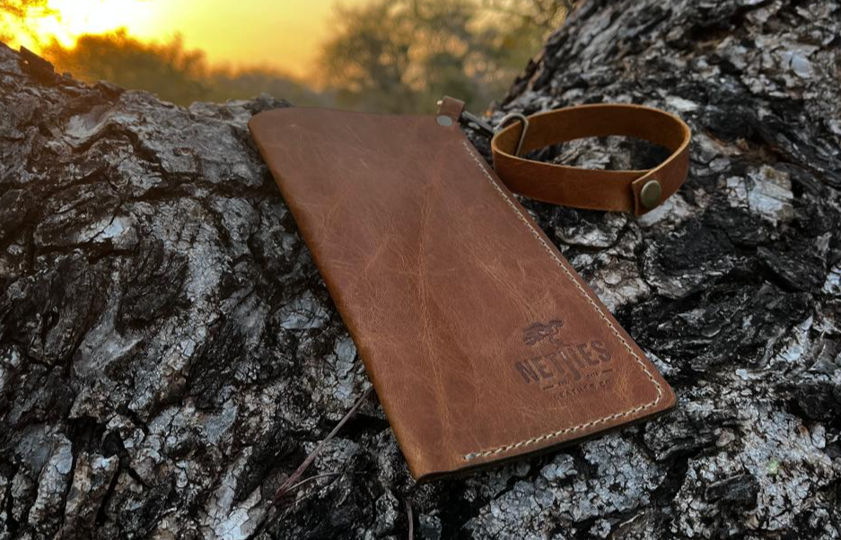 A brown leather sunglasses carrier placed outside on a tree branch with a sunset background