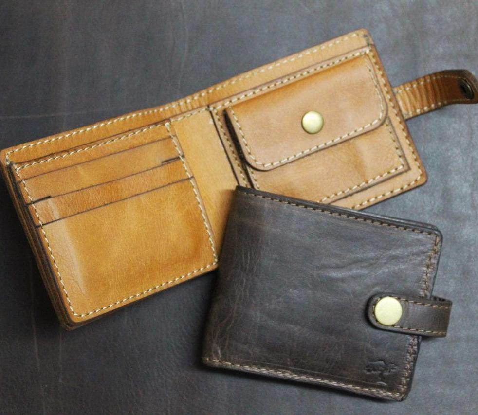 Brown and black, handmade leather wallets with a secure coin pocket, multiple card slots, and a visible brand emblem, placed on a dark surface