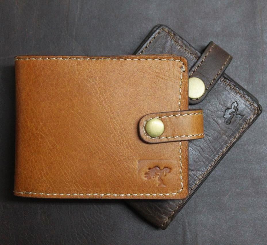 Brown and black, handmade leather wallets with a secure coin pocket, multiple card slots, and a visible brand emblem, placed on a dark surface alongside a dark-colored card.