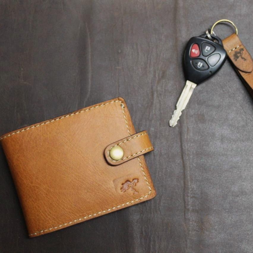 A brown, handmade leather wallet with a secure coin pocket, multiple card slots, and a visible brand emblem, placed on a dark surface next to a set of car keys