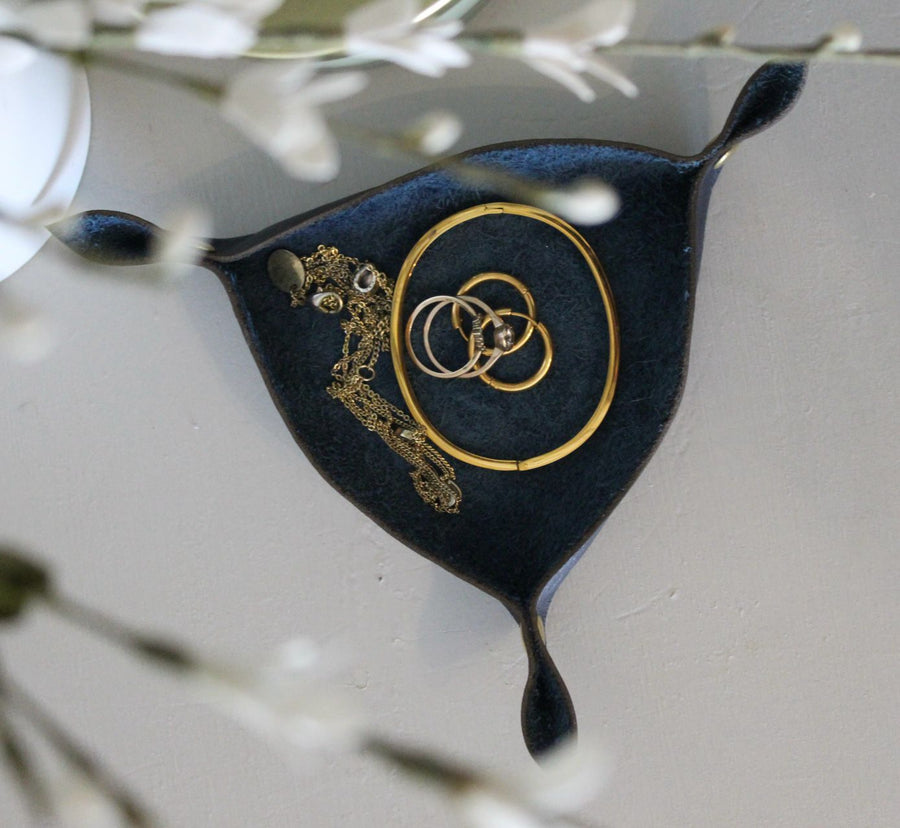 A black leather jewellery holder with a gold-tone chain and ring design, displayed on a white background with floral accents.