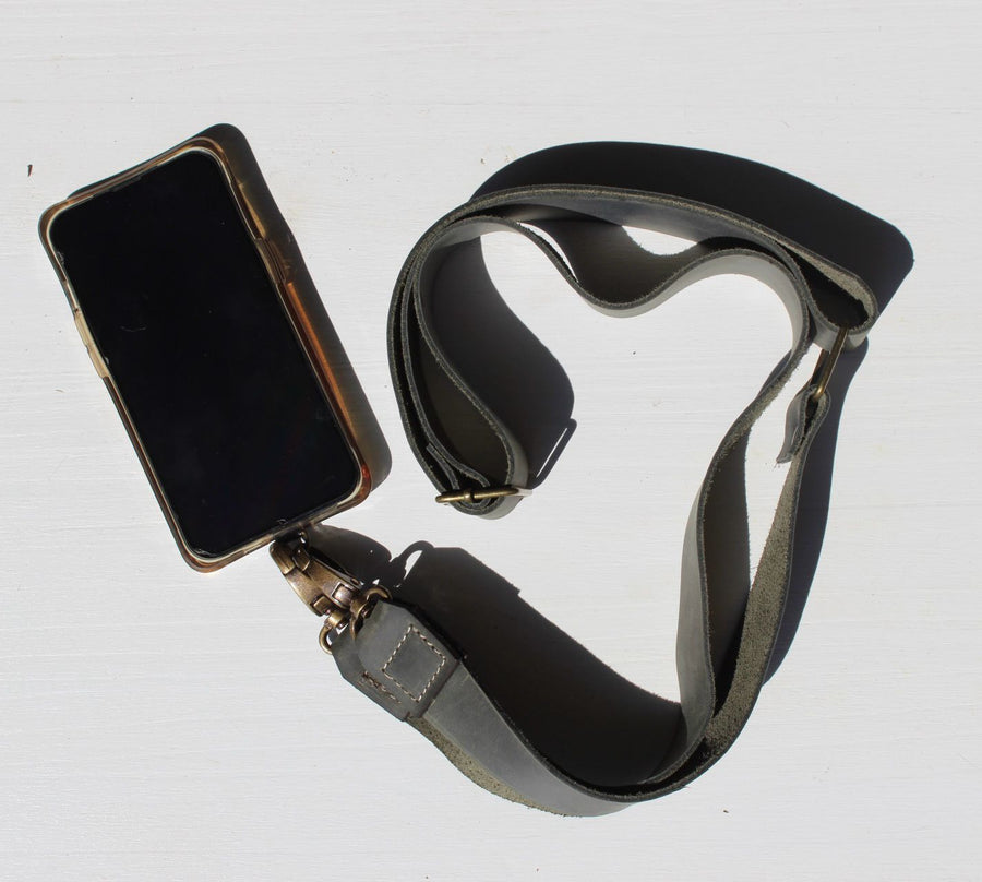 A black leather phone strap with an antique brass hardware attached to a smartphone.