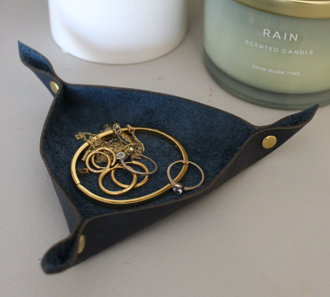 Black leather jewelry holder with golden studs on a white table next to a scented candle