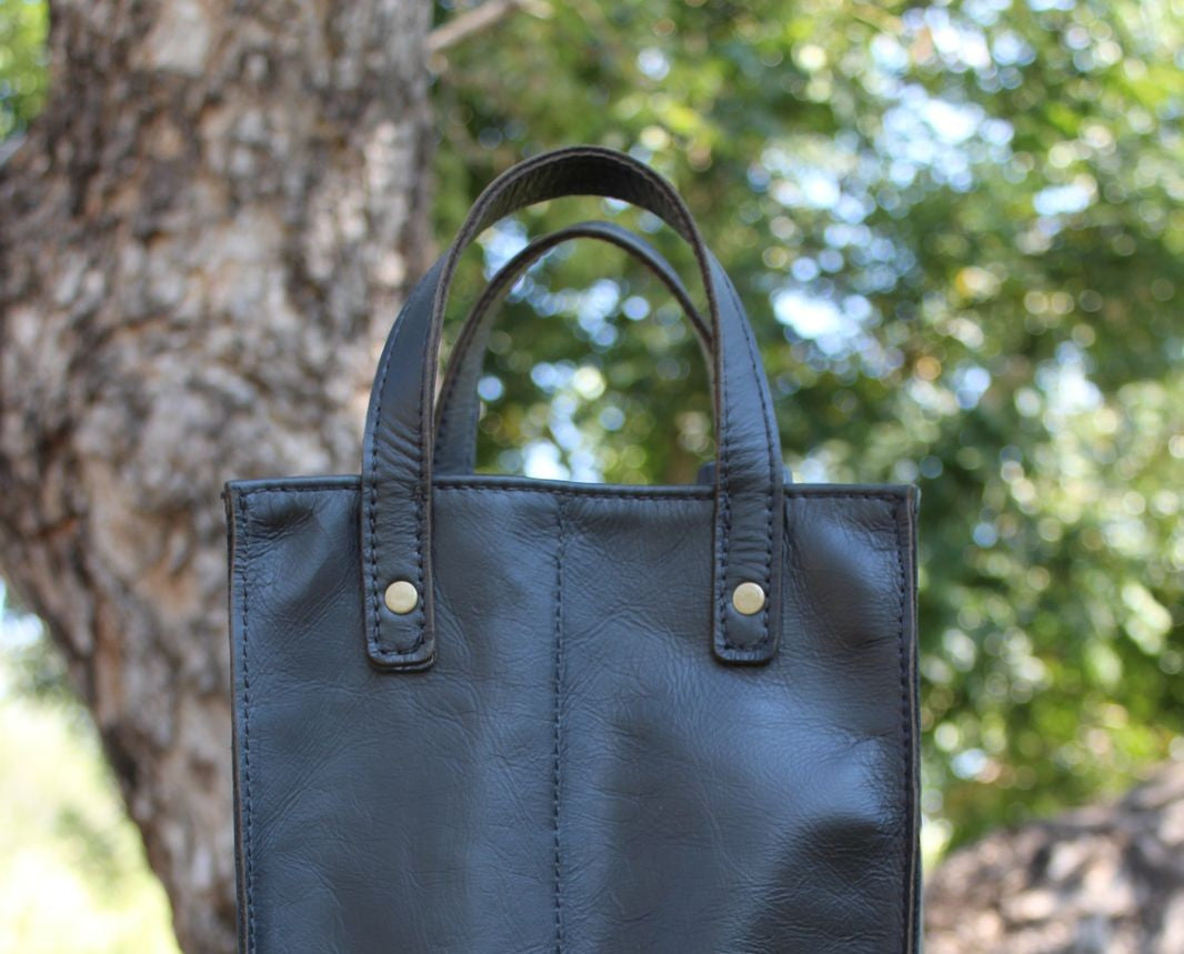 Black leather wine carry bag with black straps and brass studs, natural background