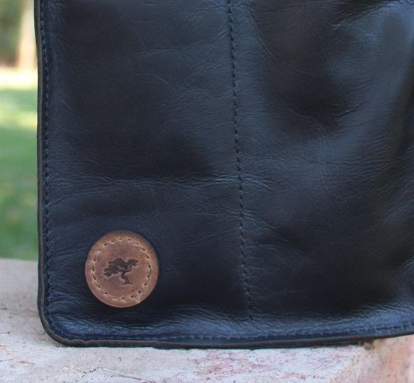 Netjies Leather Co logo on the bottom corner of a black leather wine carry bag placed outdoors on a stone surface