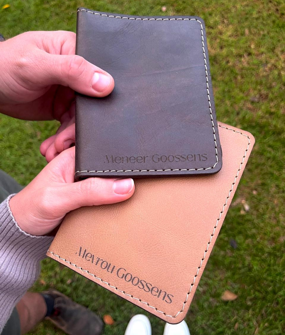 Two leather card holders, one brown and one black, held by a person against a grassy background.
