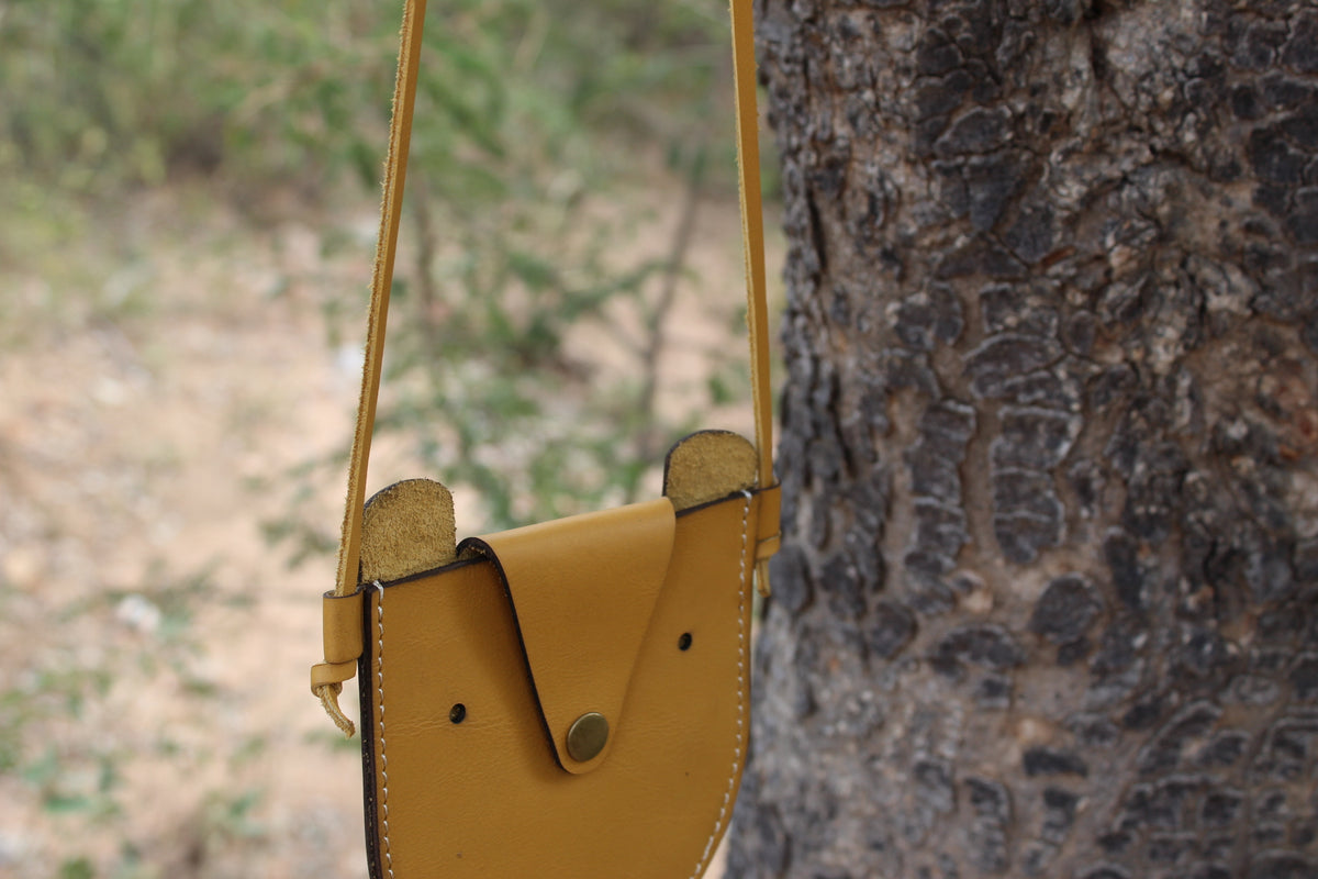 A brown leather handbag with a flap closure and a metal snap button, displayed on a tree.