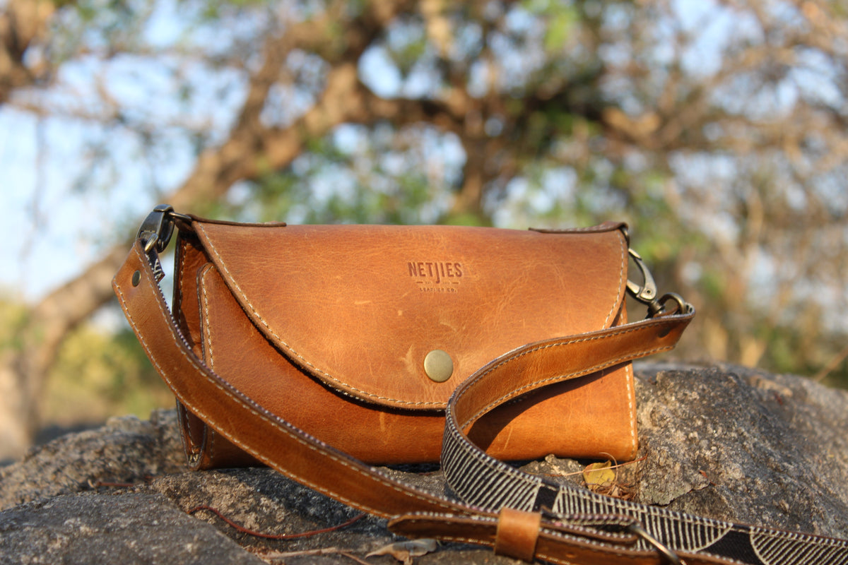 Brown leather bag with 'NETJIES' branding on a rock with blurred tree background
