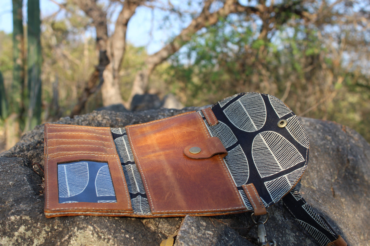 Brown leather wallet with patterned strap on a rock with natural background