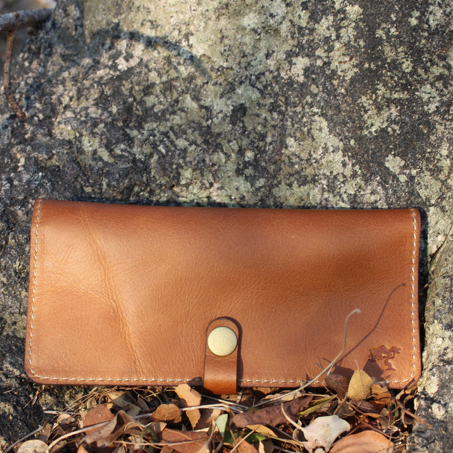 A brown leather long wallet placed on a rocky surface with fallen leaves around.