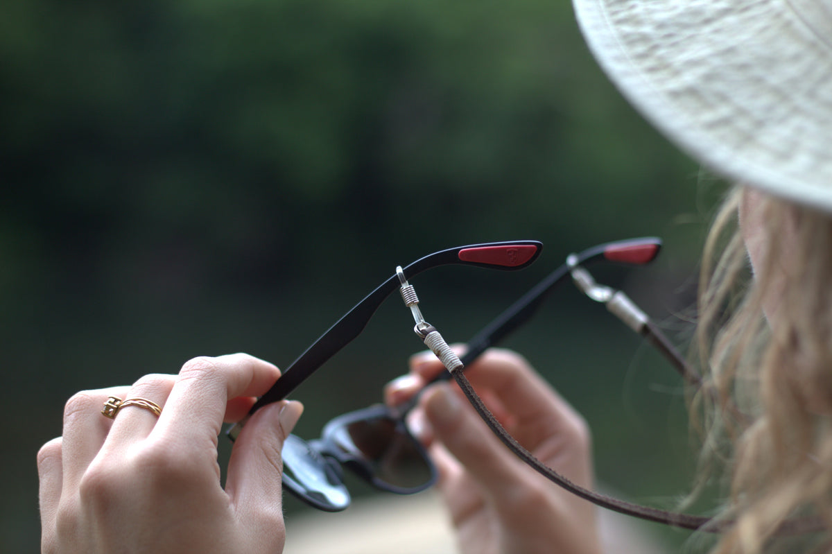 A person is adjusting their eyeglasses, which have a black frame and red accents on the arms.