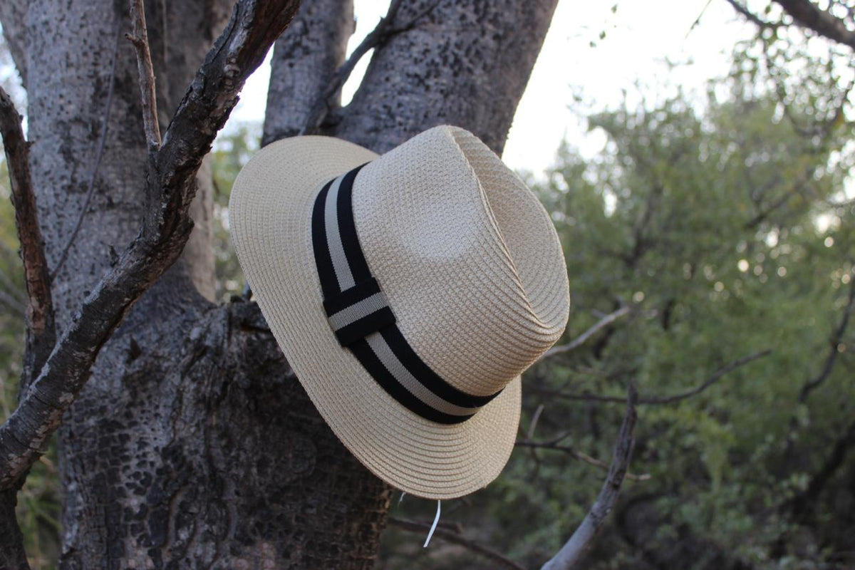 A cream-colored hat with a black and white band, hanging on a tree branch.