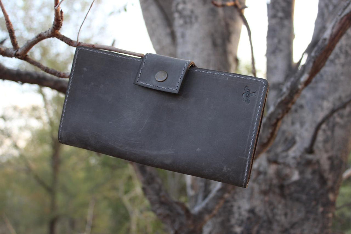 A black leather license holder hanging on a tree branch outdoors.
