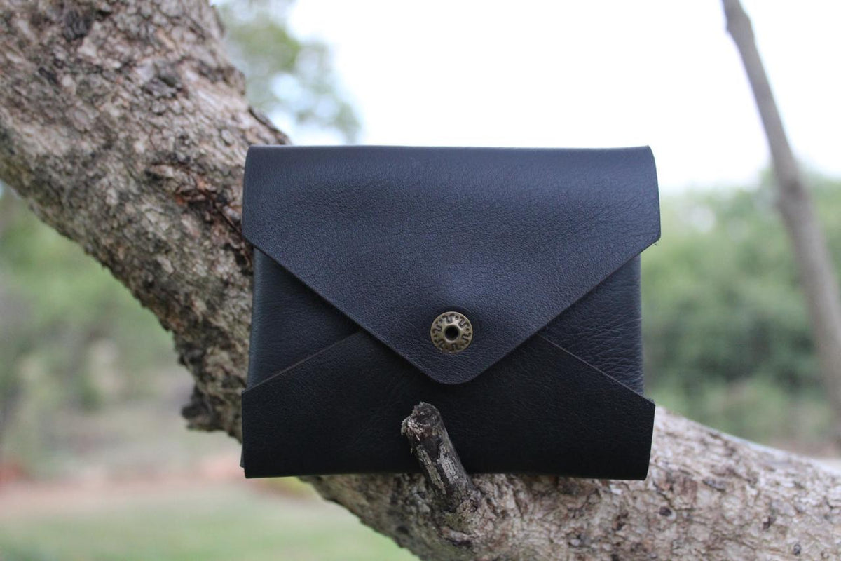 A black leather card holder with a button closure, displayed on a tree branch.