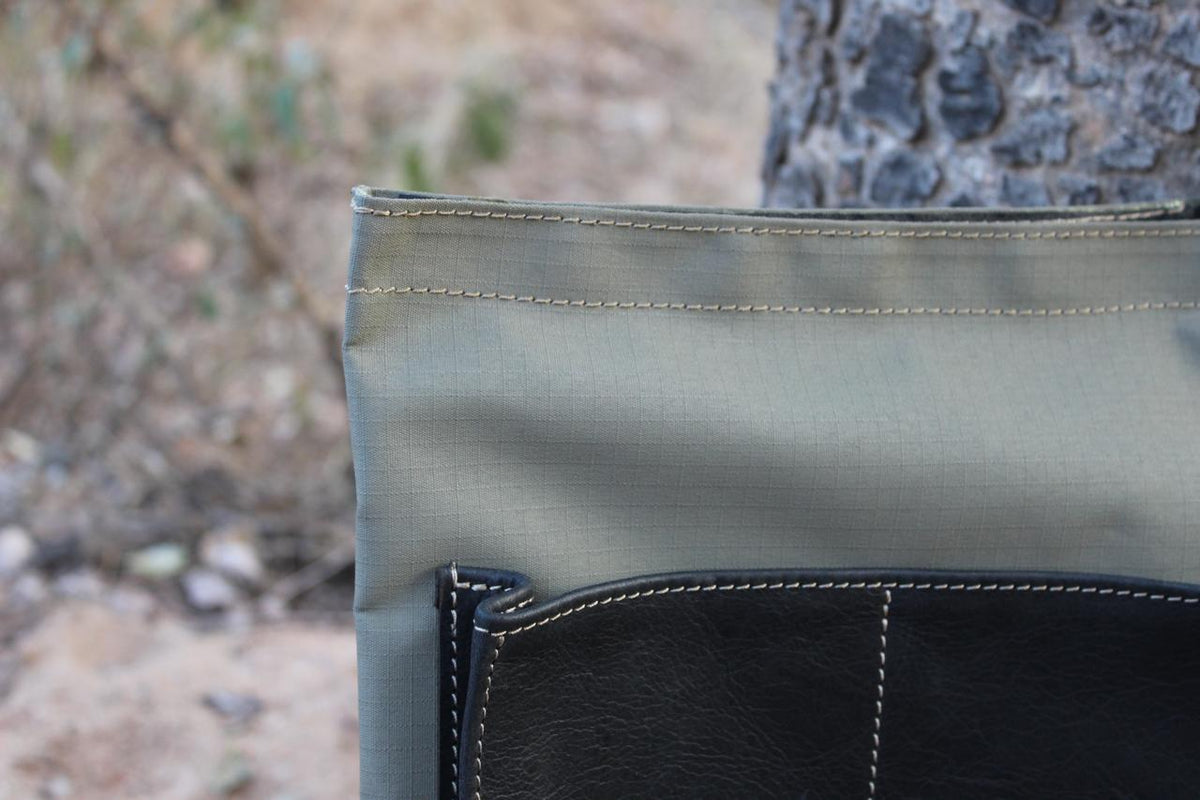 A braai bag made from green canvas and black leather with an outdoors blurred background