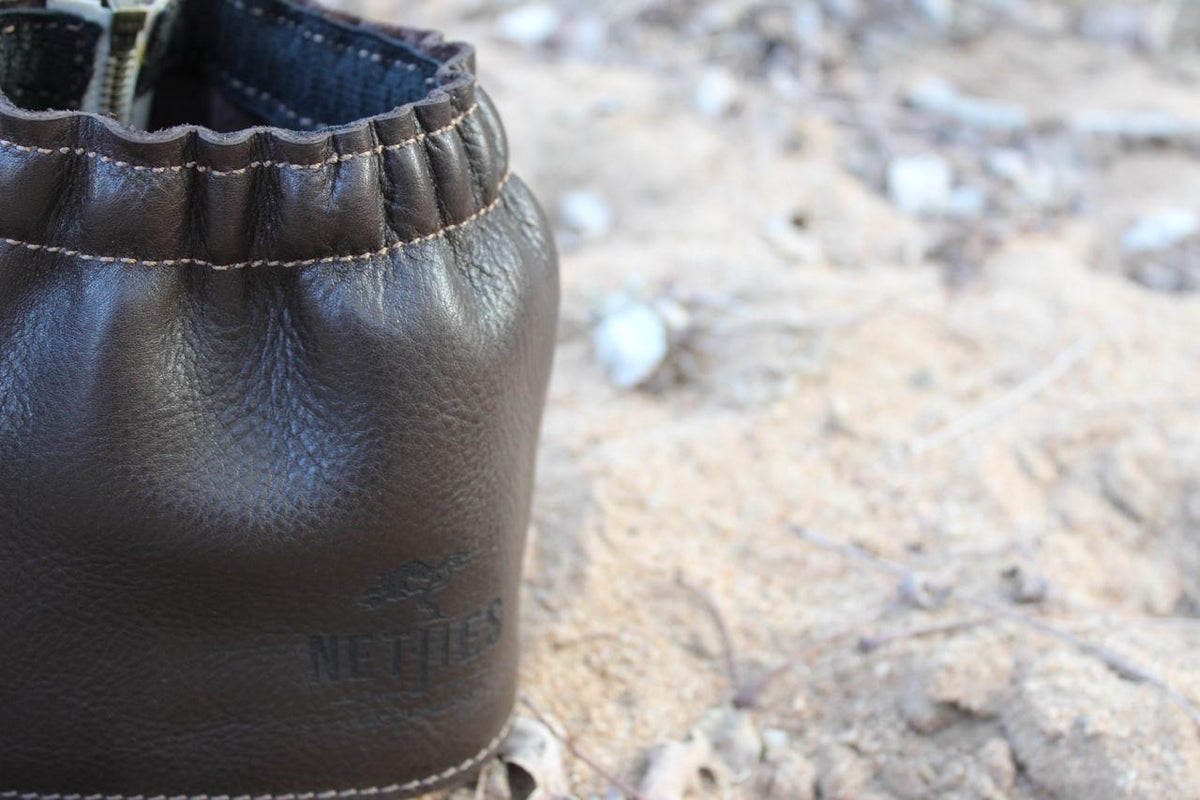 A pair of brown leather gaiters for shoes, displayed on a sandy surface.
