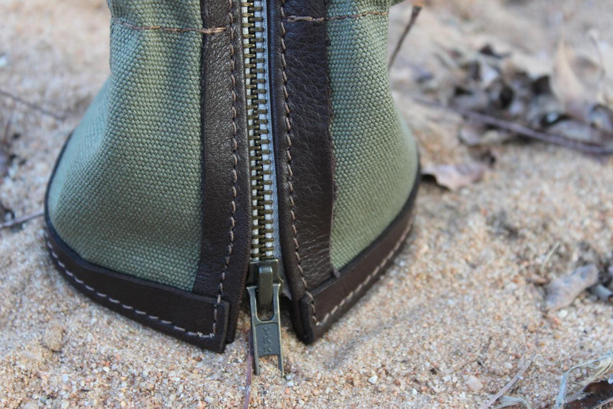 A pair of green shoe gaiters placed on a sandy surface with natural surroundings.