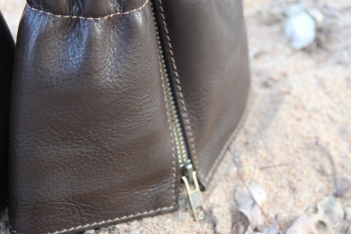 A pair of brown leather gaiters for shoes, displayed on a sandy surface.