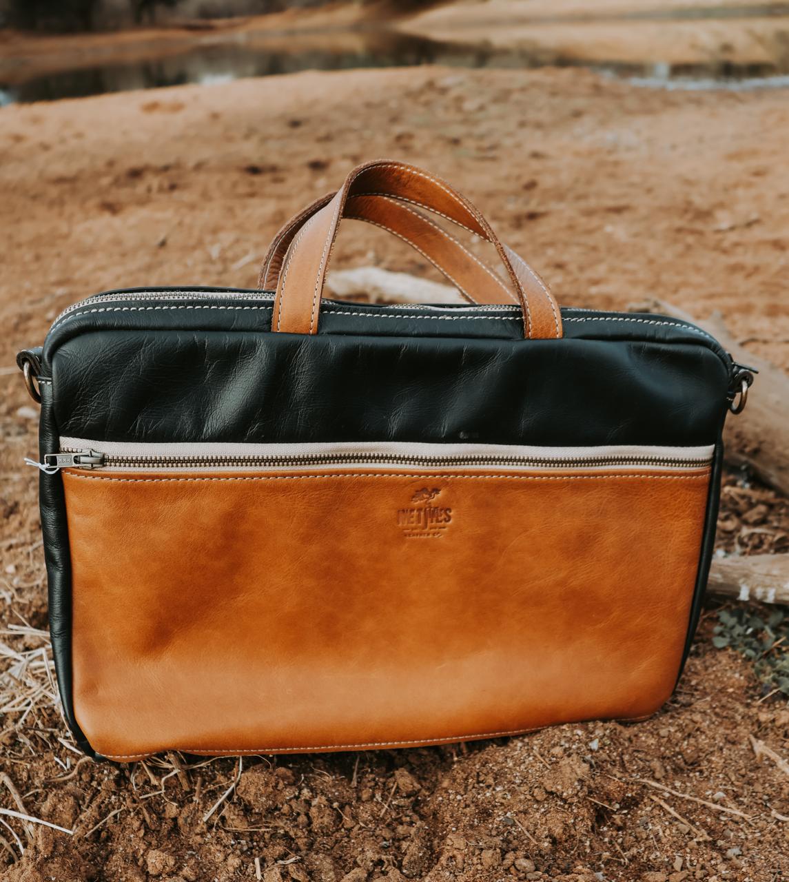Two-tone leather briefcase with black top section and brown bottom section on a natural background