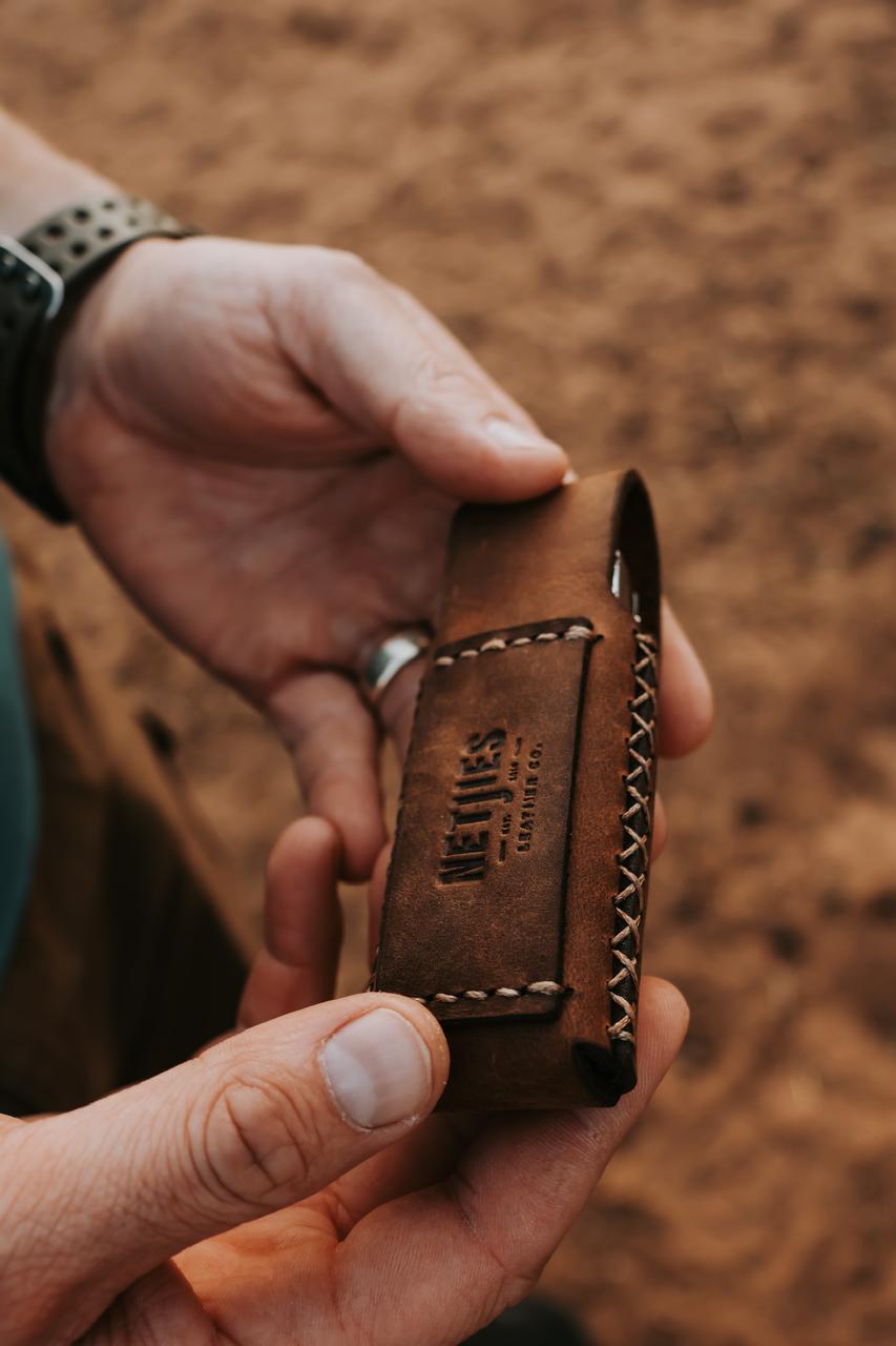 Person holding a brown leather multitool pouch with visible branding against a blurred brown background