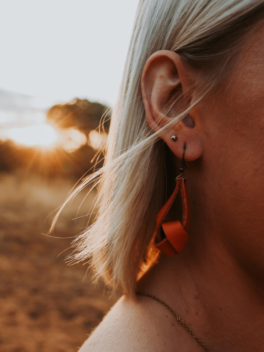Close-up of a person wearing orange leather earrings with a blurred natural background
