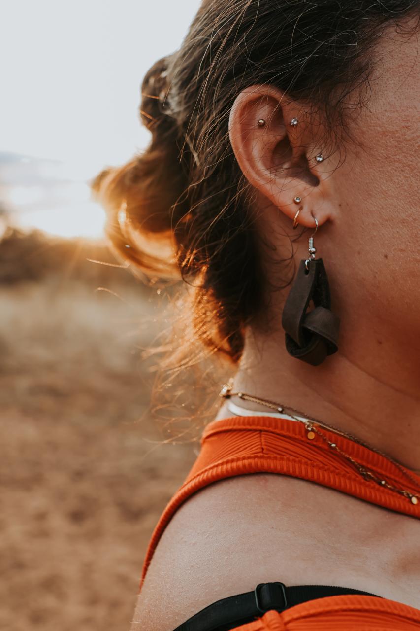 Close-up of a person wearing black leather earrings with a blurred natural background