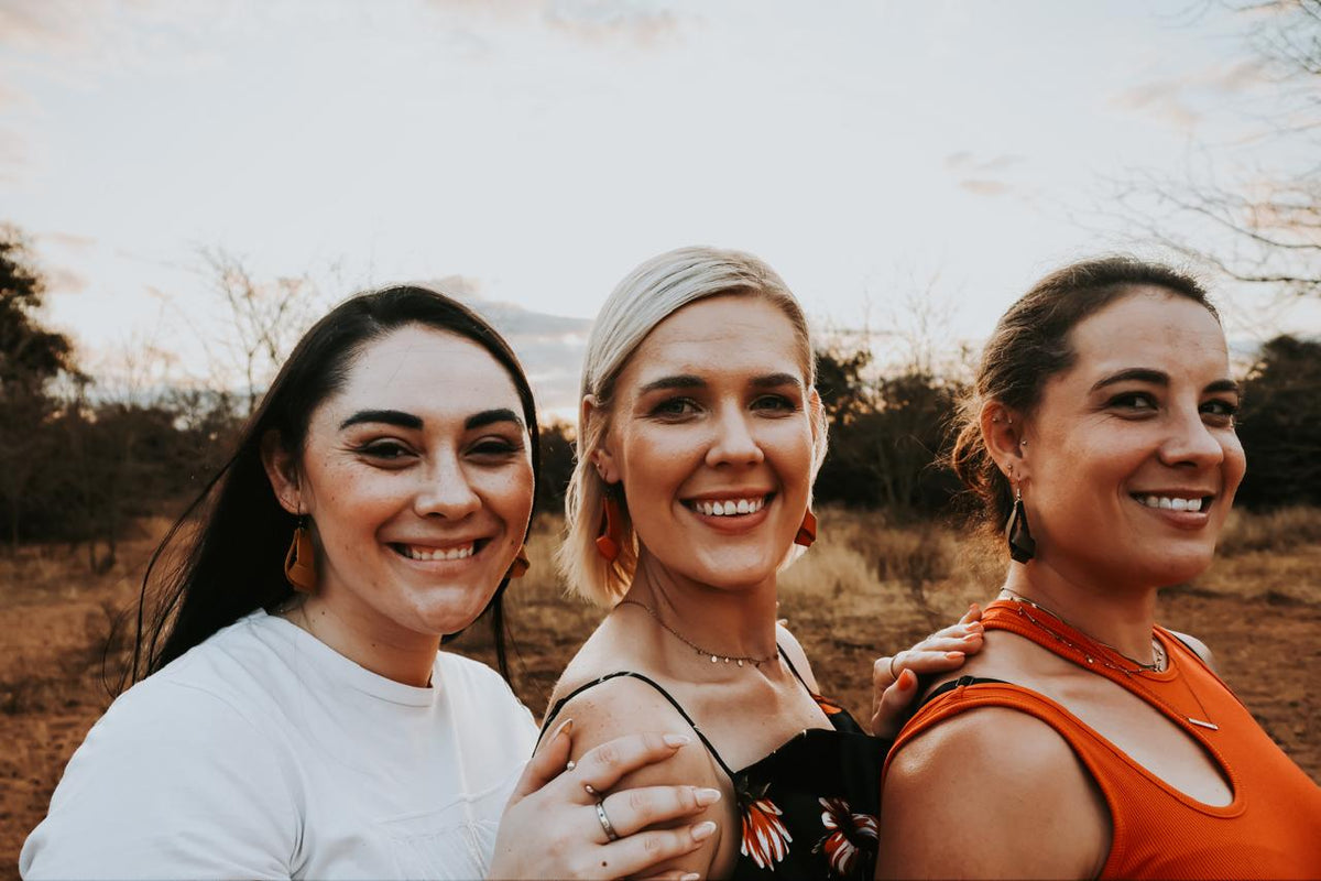 Three women standing together in a field wearing leather earrings with a blurred background