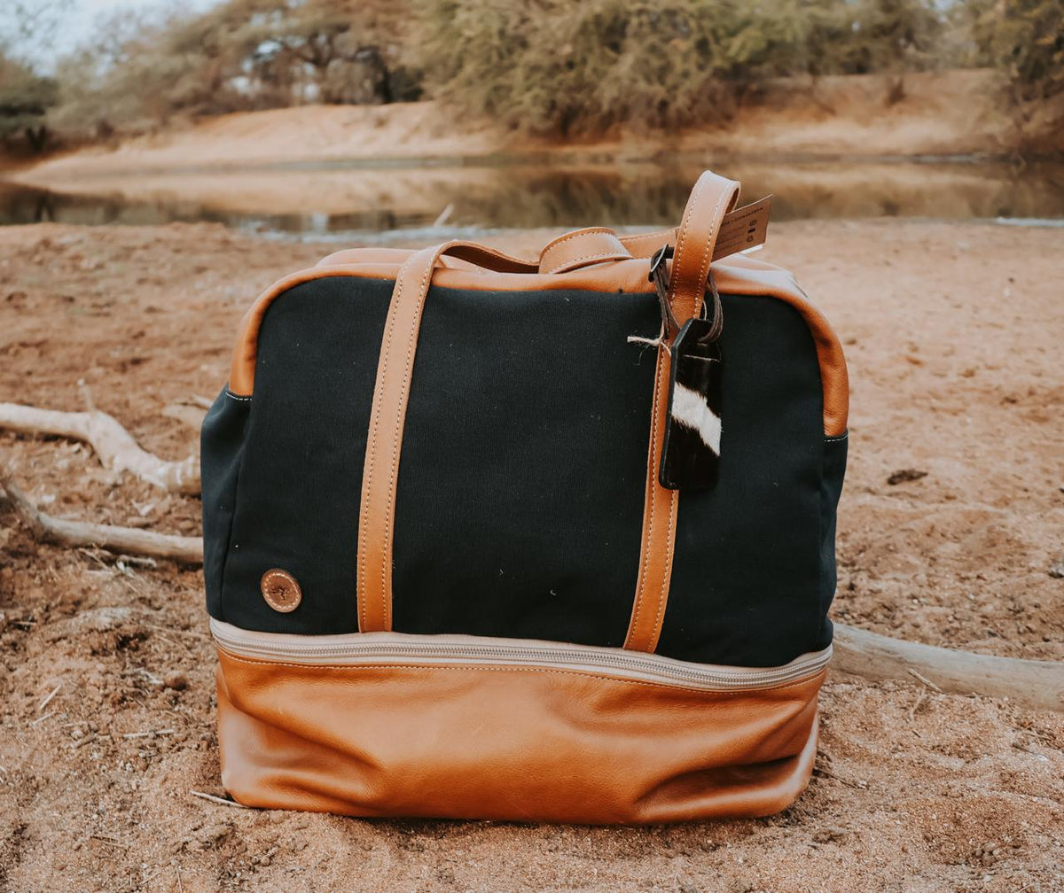 Black and brown duffel bag on sandy ground with natural background