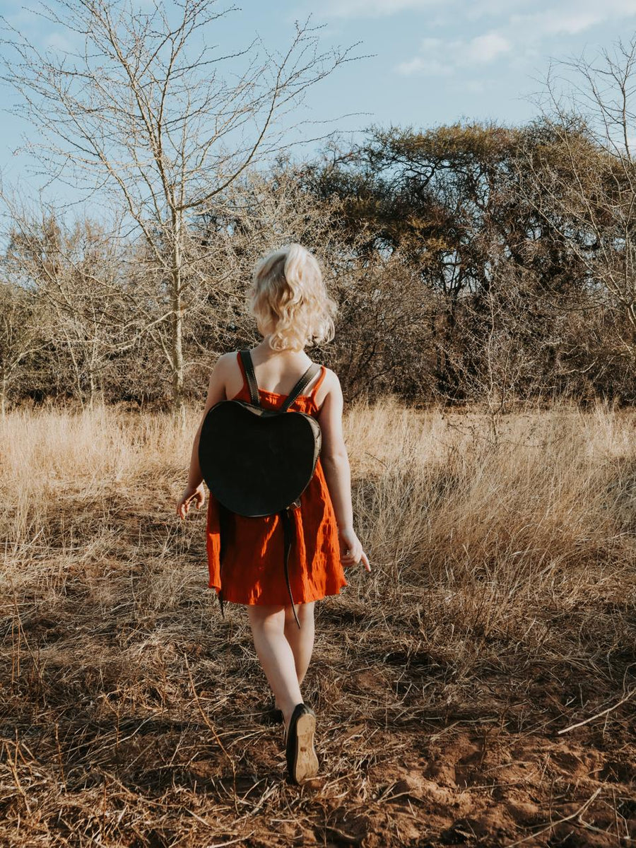 Woman in an orange dress walking through a dry, leafless field with a black bag.