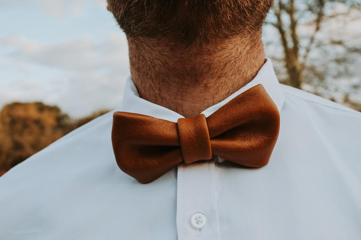 Brown leather bow tie worn by a person with a blurred natural background