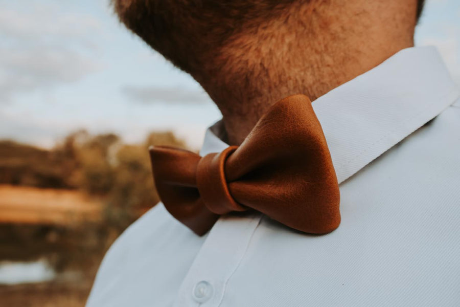 Brown leather bow tie worn by a person with a blurred natural background