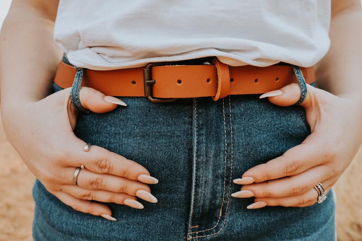 Person wearing a white shirt, blue jeans, and an orange belt with a blurred background