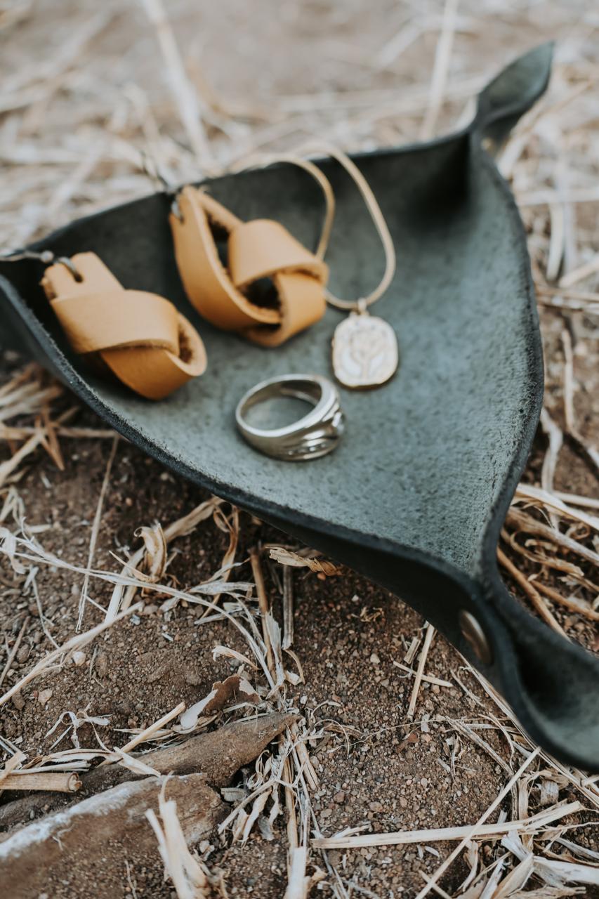 Jewelry set including a ring, necklace, and leather pieces in a black leather jewelry holder placed on the ground outdoors.