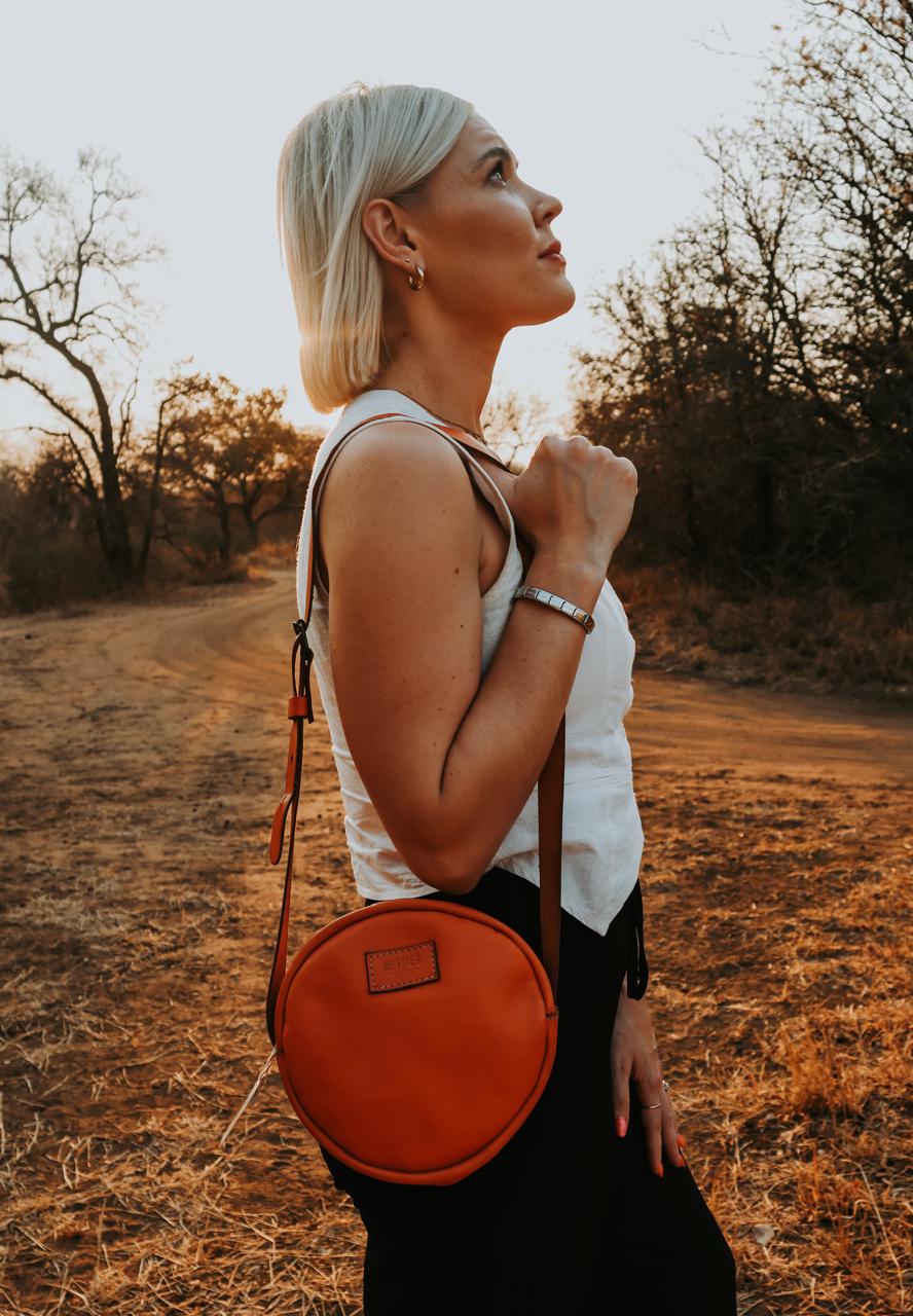 Woman with a round orange bag standing in a natural setting