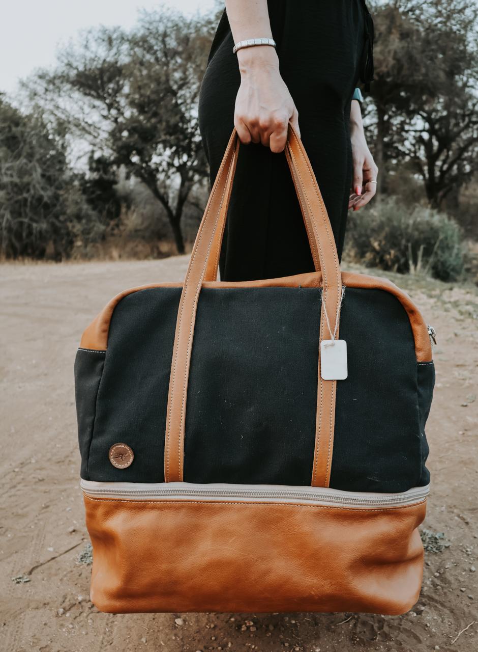 Person holding a black and brown bag outdoors with trees in the background