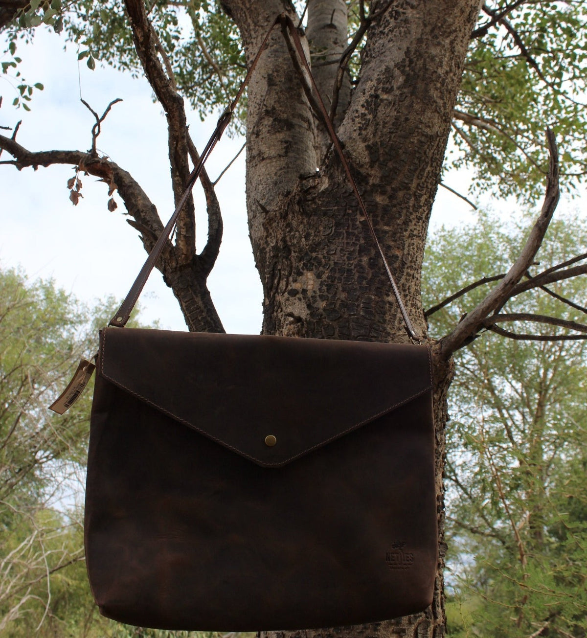 A brown leather laptop sling hanging from a tree branch.