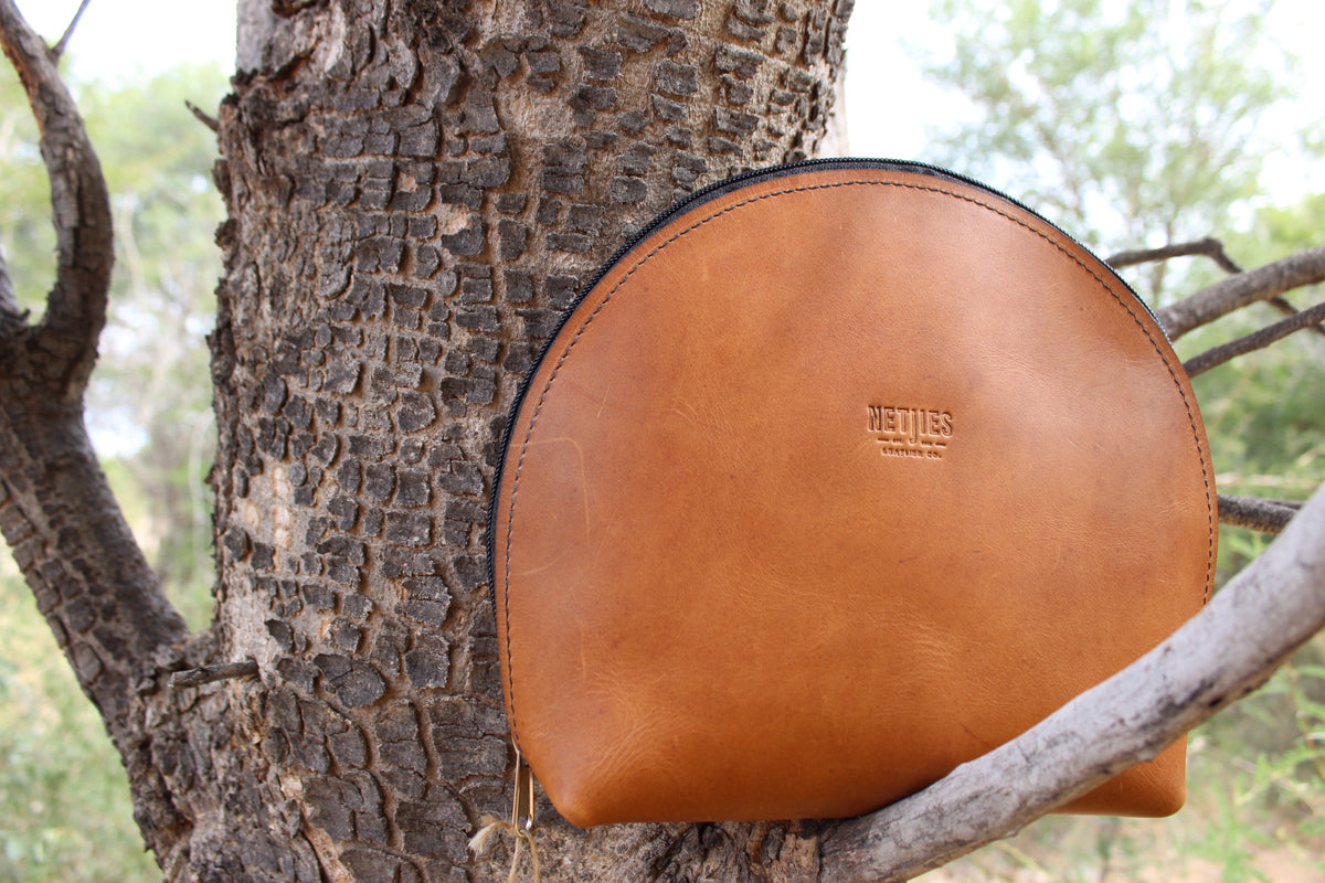 A brown make-up bag placed on a tree branch outdoors.