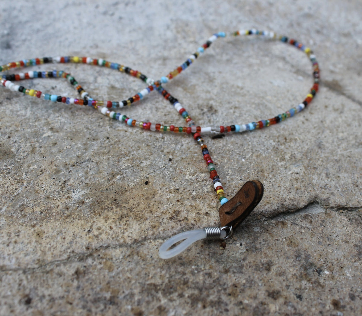 A beaded toutjie with a variety of colorful beads laid out on a rocky surface.